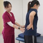 One Spine practitioner in maroon scrubs assessing lower back movement with a Malaysian patient in clinic