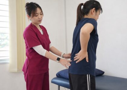 One Spine practitioner in maroon scrubs assessing lower back movement with a Malaysian patient in clinic